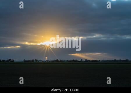 Sun peeks through the clouds. Beautiful sun beams or crepuscular rays over the landscape. Stock Photo