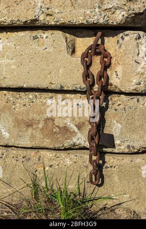view on old rusty chain with open padlock hanging at a concrete wall in warm evening sunset light Stock Photo