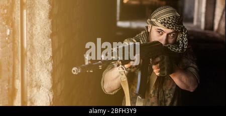 Arab male soldier in a headdress from the national keffiyeh with a weapon in his hands. Muslim man with a gun on a black background. Stock Photo