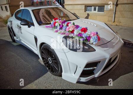 Decorated with flowers as for a wedding . Fresh flowers on the car. Beautiful wedding bouquet on white wedding car . Beautiful wedding car. Front of Stock Photo