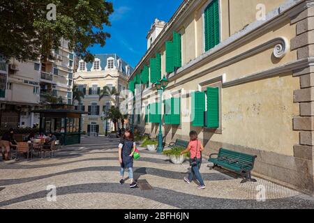 People walking on a narrow pedestrian cobblestone street in the historic district of Macau, China. Stock Photo