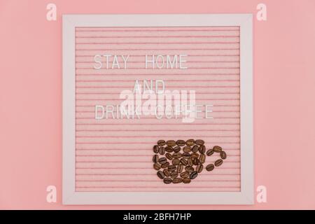 Quote stay home and drink coffee on pink decorative board. Cup made of coffee beans. Prevention tagline form covid-19 Stock Photo