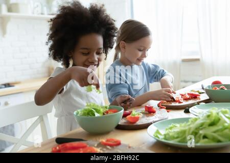 Excited little multiethnic sisters cooking in kitchen together Stock Photo