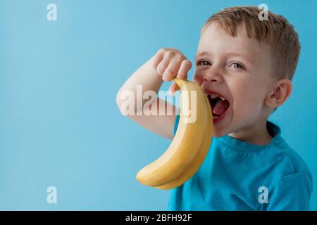 Little Boy Holding and eating an Banana on blue background, food, diet and healthy eating concept Stock Photo