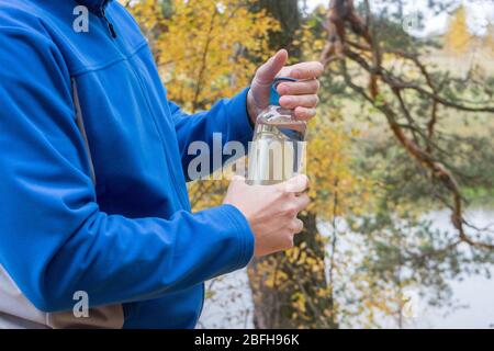 Thirsty man opens sports water bottle after outdoor workout in autumn. fitness, sport, people and lifestyle concept. Stock Photo