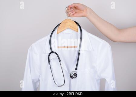 Job vacancy concept. Cropped close up photo of hand holding white doctor coat on hanger isolated over grey background Stock Photo