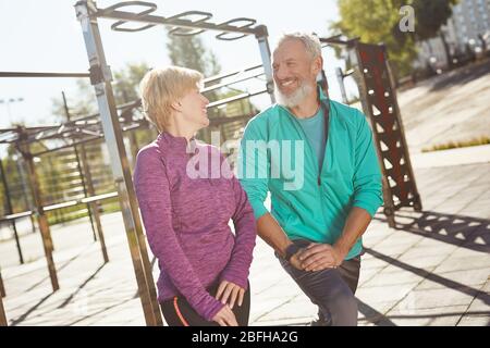 Warming up. Happy mature family couple in sportswear doing gymnastics together at the stadium. Man and woman doing stretching exercises outdoors Stock Photo