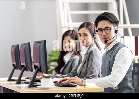 Young adult friendly and confidence operator asian man agent with headsets working in a call center with his colleague team working as customer servic Stock Photo