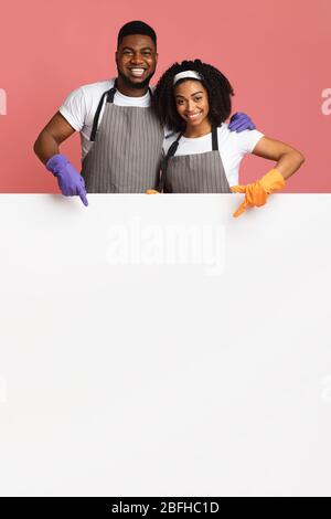 Couple Of Cleaners In Aprons And Gloves Pointing At White Board Stock Photo