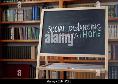 Inscription social distancing stay at home. Outbreak Warning. written white chalk on blackboard in connection with epidemic of coronavirus worldwide. Stock Photo