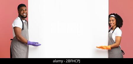 Positive Couple In Gloves And Aprons Pointing At White Advertisement Board Stock Photo