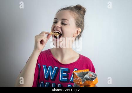 Smiling young Caucasian woman girl eating biting potato chips crisps Stock Photo