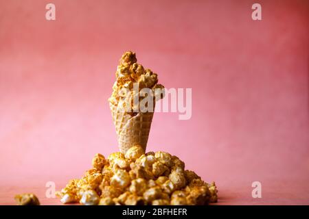 Caramel Popcorn in ice cream cone on pink colorful background. caramel Popcorn on a cone cornucopia. Splitted popcorn on bright hipster background Stock Photo