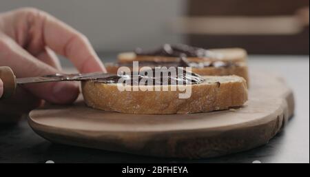 man spreading chocolate spread on ciabatta slice on olive board Stock Photo