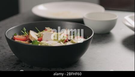 almond flakes falling on salad with chicken, arugula and tomatoes in black bowl Stock Photo