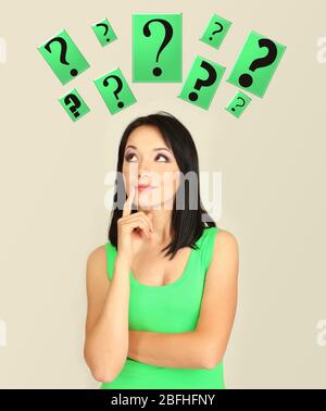 Girl thinking surrounded by question marks on beige background Stock Photo