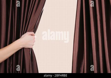 Hand opening curtain on beige background Stock Photo