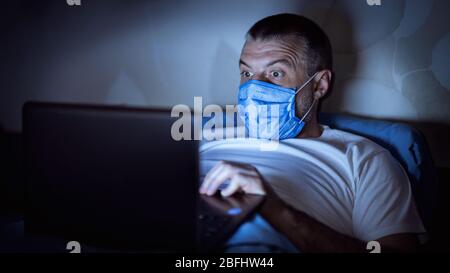 Man Reading News On Laptop Lying In Bed At Night Stock Photo