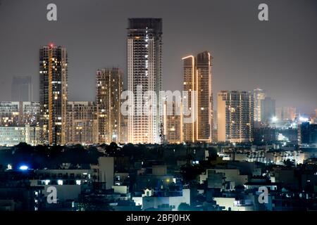 High rise multi story skyscrapers lit up at night with small houses in the foreground at night in gurgaon delhi Stock Photo