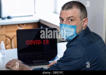 Man Sitting At Laptop With Word COVID-19 On Screen Indoors Stock Photo
