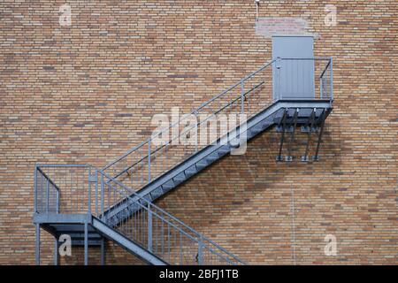 Exterior steel staircase leading to a closed door on a red brick building wall. Concept for construction and industry, structure and architecture, cli Stock Photo