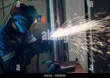 Man in mask cuts metal with plasma cutter. Helmet and spakrs. Stock Photo