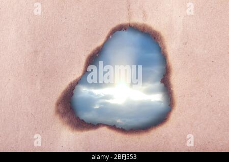 Blue sky background with clouds through hole in craft paper Stock Photo