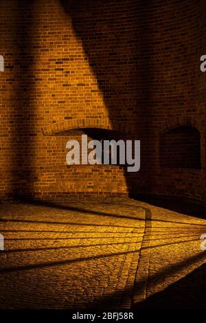 Light and shadow on cobblestone street and sidewalk inside barbican fortification at night in Old Town of Warsaw in Poland, illumination coming from a Stock Photo