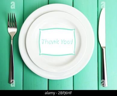 Plate with text "Thank you", fork and knife on color wooden background Stock Photo