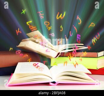 Many books with flying letters on table on bright background Stock Photo