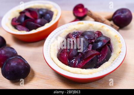 Traditional German glazed plum tartelettes in miniature pie dishes with cinnamon sticks Stock Photo