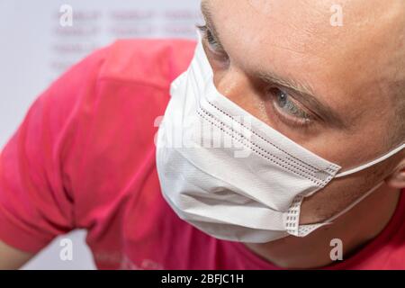 Close up of a man wearing white medical mask, thoughtful expression on his face clutched head. A bald man in his thirties. Stock Photo