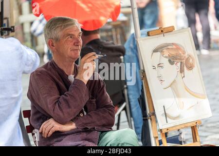 Portrait of a male artist smoking beside one of his artworks sitting on an easel at the artists market in Montmartre, Paris Stock Photo