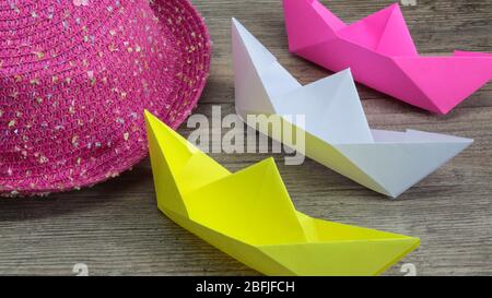 Origami, colorful boats and pink hat on wooden background, hobby Stock Photo