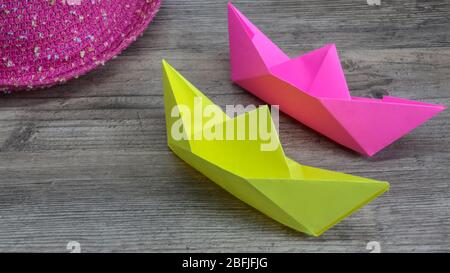 Origami, colorful boats and pink hat on wooden background, hobby Stock Photo