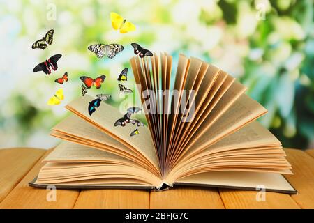 Open book on wooden table and butterflies on natural background Stock Photo
