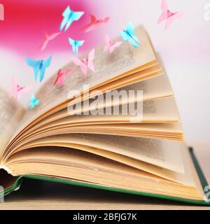 Open book on table and paper butterflies on bright pink background Stock Photo
