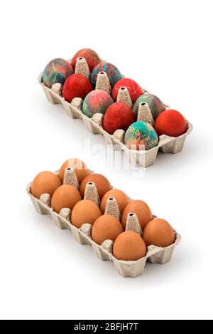 Packs of regular eggs and Colorful Easter eggs in cardboard egg box on white background. Raw chicken eggs in open egg box on a white background Stock Photo