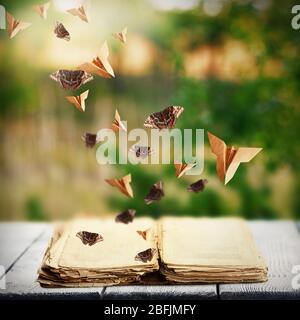 Open book on wooden table and butterflies on natural background Stock Photo