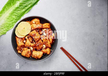 Korean Sweet Fried Chicken Dakgangjeong in black bowl at grey concrete background. Dakgangjeong is korean cuisine dish with deep fried crunchy chicken Stock Photo
