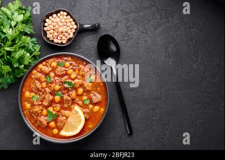 Moroccan Harira Soup in black bowl at dark slate bakcground. Harira is Moroccan Cuisine dish with lamb or beef meat, chickpeas, lentils, tomatoes, cil Stock Photo
