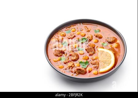 Moroccan Harira Soup in black bowl isolated on white bakcground. Harira is Moroccan Cuisine dish with lamb or beef meat, chickpeas, lentils, tomatoes Stock Photo