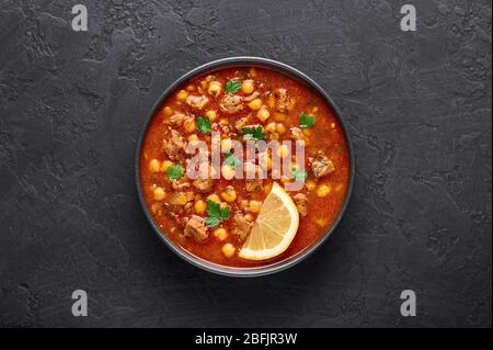 Moroccan Harira Soup in black bowl at dark slate bakcground. Harira is Moroccan Cuisine dish with lamb or beef meat, chickpeas, lentils, tomatoes and Stock Photo