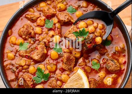 Moroccan Harira Soup in black bowl. Harira is Moroccan Cuisine dish with lamb or beef meat, chickpeas, lentils, tomatoes, ciliantro. Ramadan Iftar Foo Stock Photo