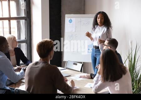 Biracial female speaker present business project on flip chart Stock Photo