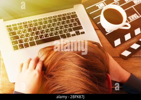 Head of tired scriptwriter on laptop at wooden desk background Stock Photo