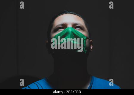 Young white man wears a green medical mask during quarantine at his home to prevent getting the flu , overhead light, Bogotá, April 18, 2020 Stock Photo