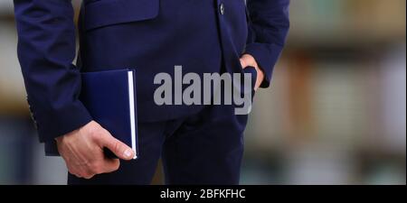 Male hand holding book on blurred bookshelves background Stock Photo