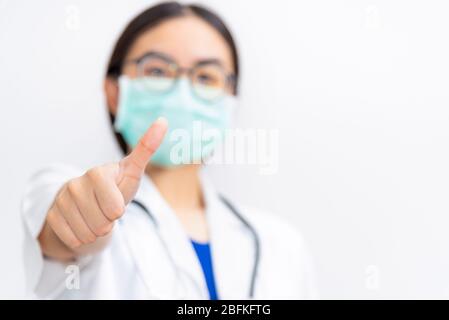 Asian young woman doctor wear mask to safety Coronavirus, Closeup physician show thumb up to support a patient in the fight against disease epidemic C Stock Photo