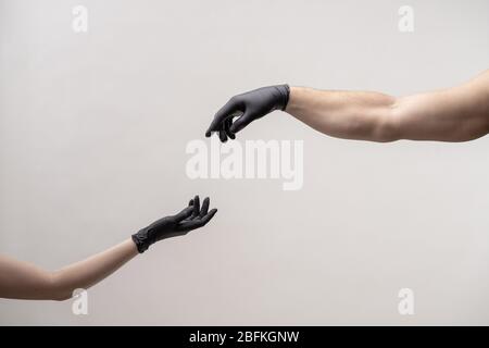 Hands in black silicone gloves stretches to each other to touch Stock Photo